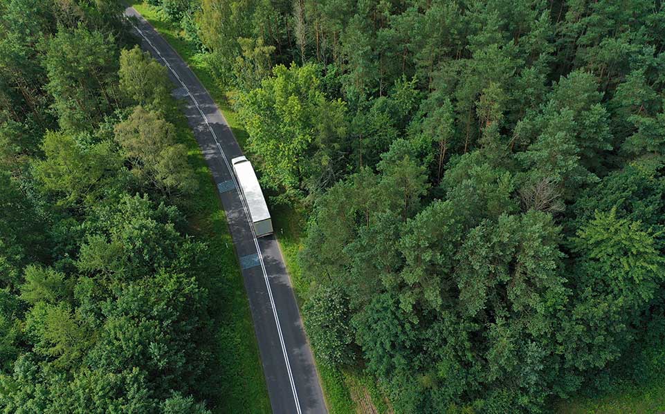 A tractor trailer driving down a forest highway.