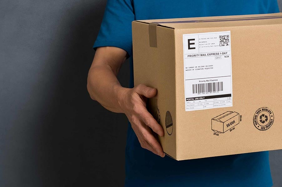 An image of a person holding a cardboard box and shipping label.