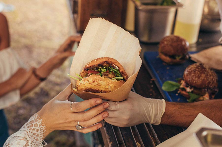 An image of a sandwich wrapped in paper being passed to a customer.