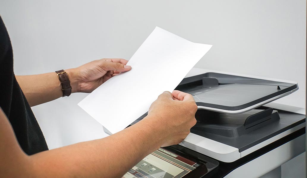 An image of a person holding paper next to a copier.