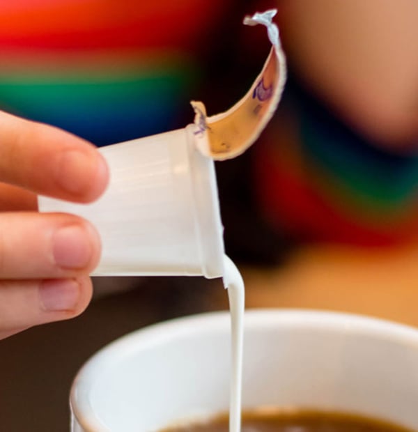 Opened creamer cup being poured into coffee